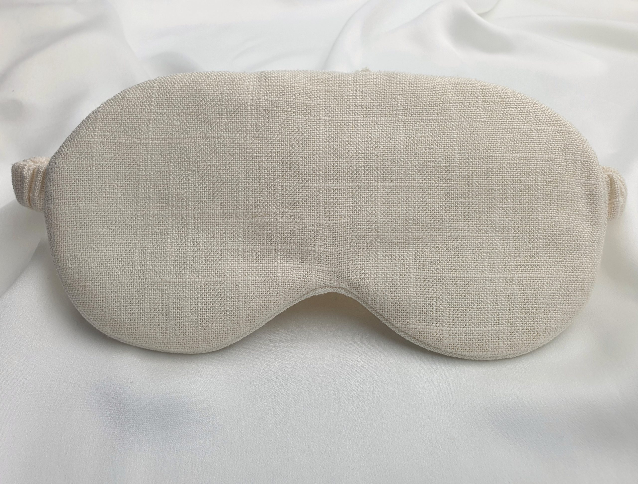 Soft ivory sleep mask made from natural linen and silk on a silk background