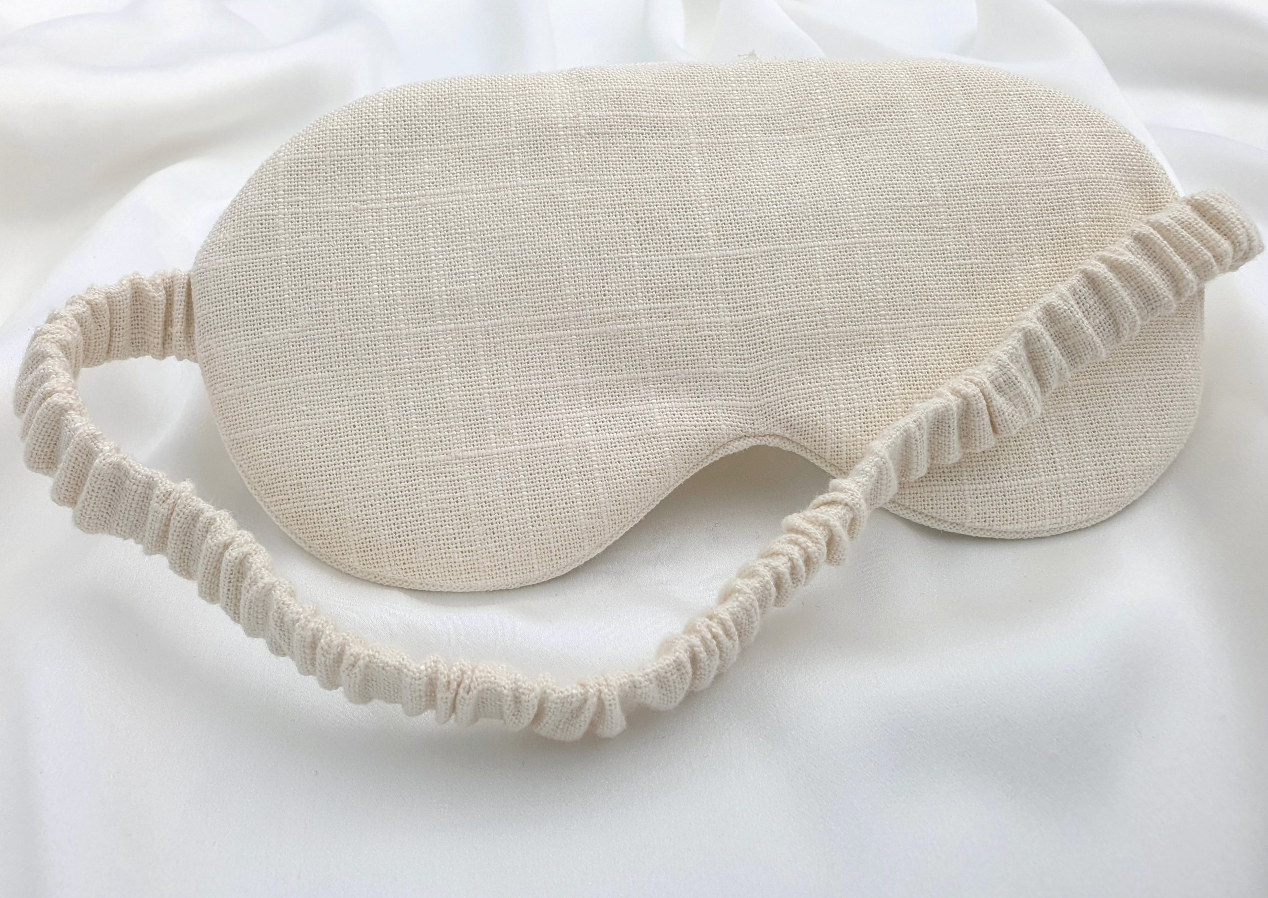 Ivory linen sleep mask with elastic band on soft silk background